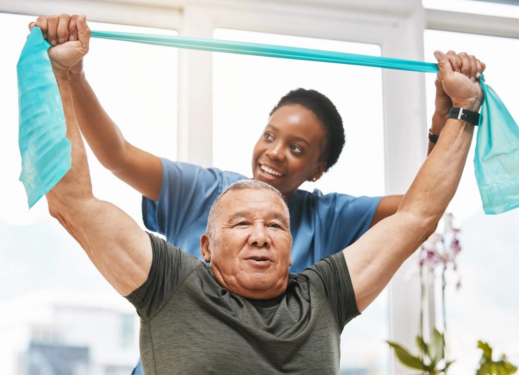 An older gentleman receives physical therapy and rehabilitation with the aid of a stretching band, under the supervision of a woman doctor.