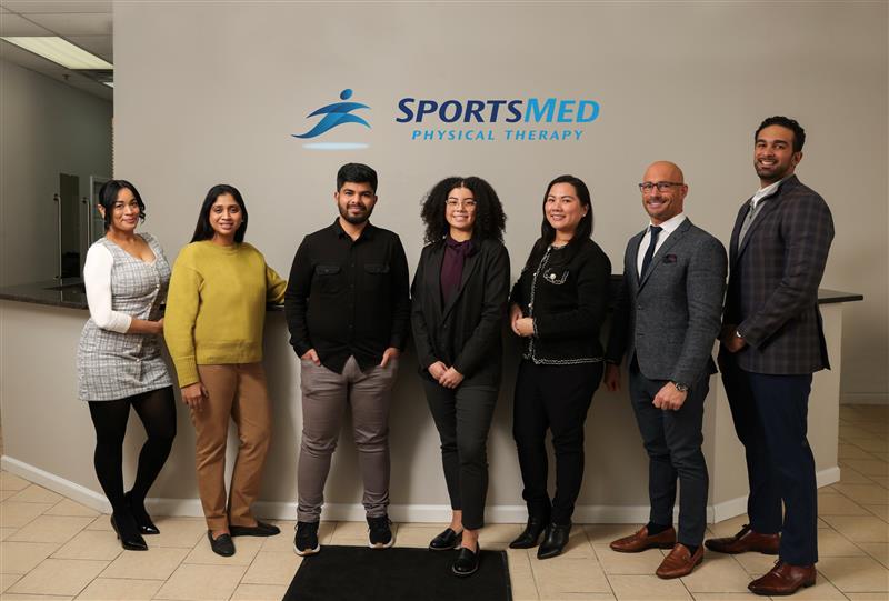 Image of a group of people standing together in front of a SportsMed Physical Therapy logo