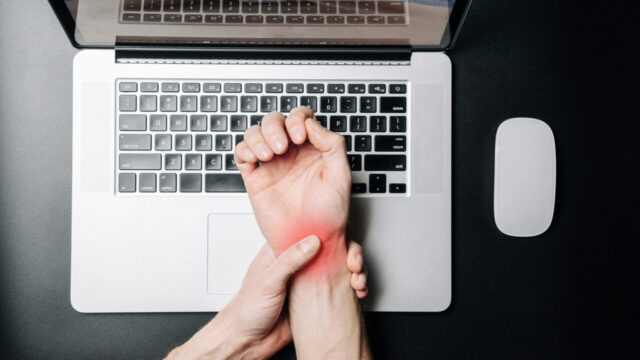 Man holding painful injury wrist in front of computer