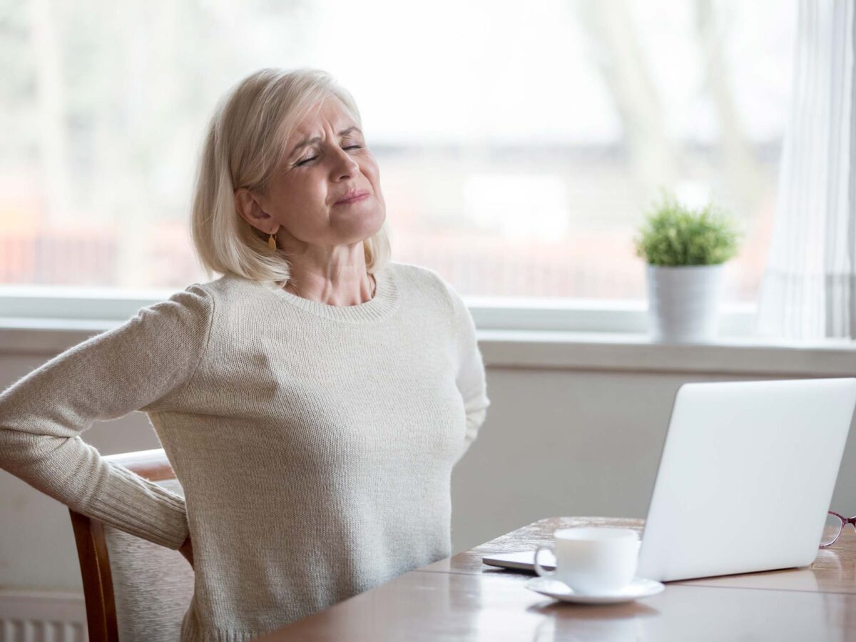 Woman at table touching her back in pain.