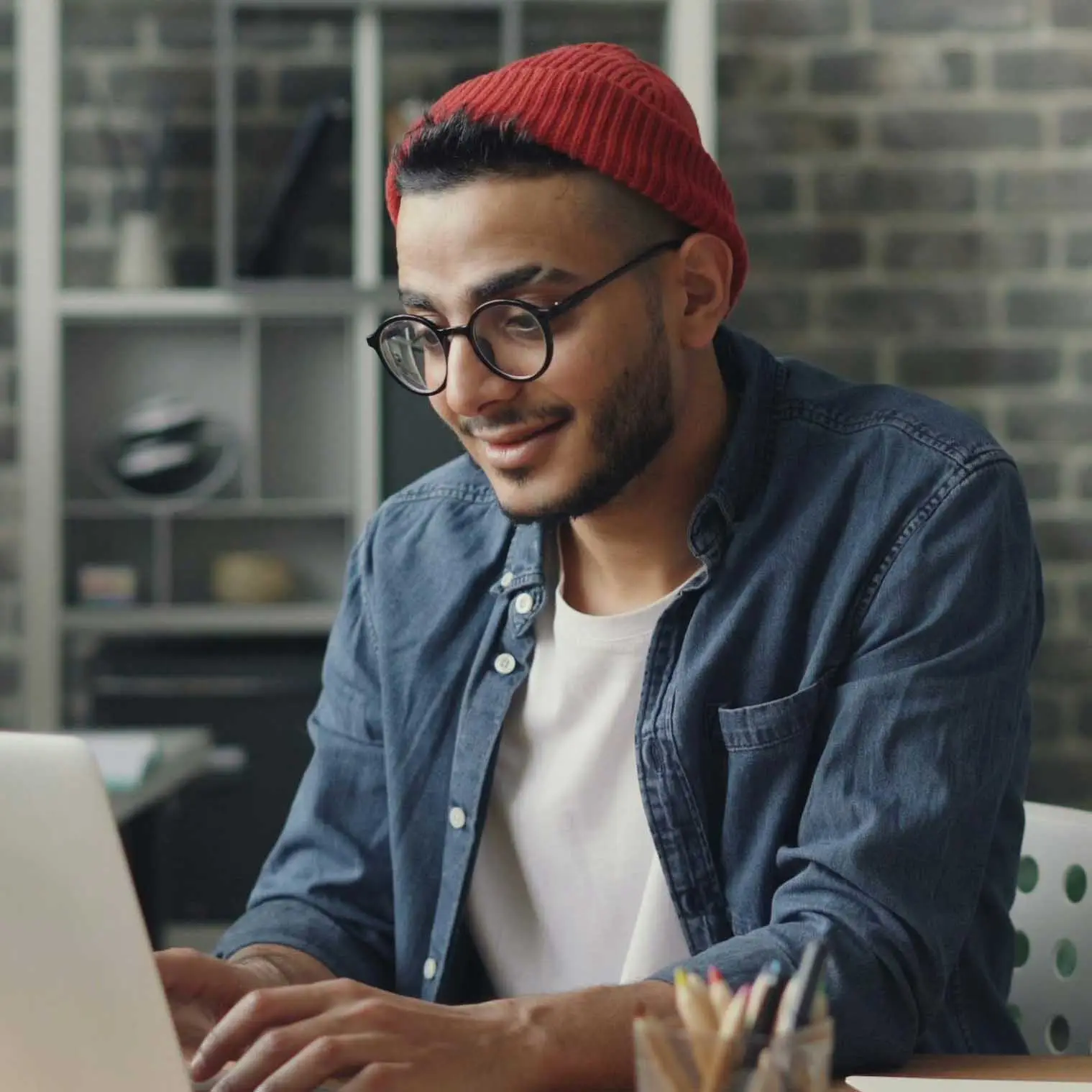 Man wearing a beanie working at a laptop on a desk.
