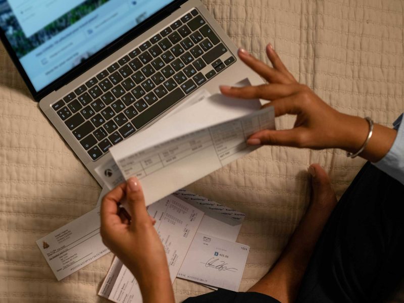 someone opening a group of envelopes with bills in them while sitting in front of a laptop computer.