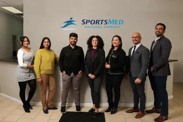 Image of a group of people standing together in front of a SportsMed Physical Therapy logo
